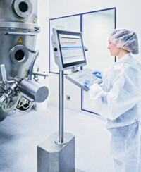 Person with a protective overall in a lab stands in front of a device where PAS-X MES is displayed